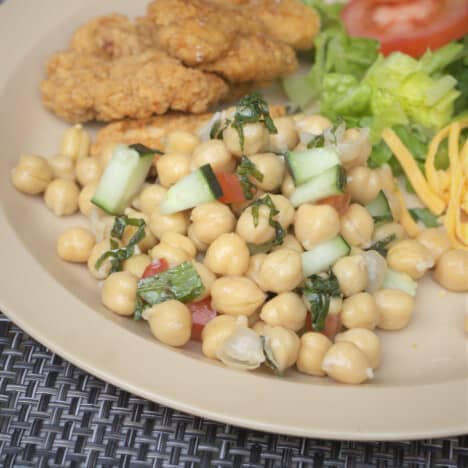 Chickpea salad served on a plate as part of a larger meal including chicken tenders and salad.