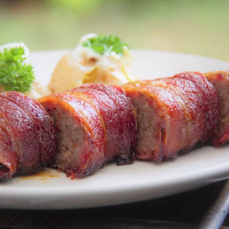 Sliced bacon-wrapped sausage sits on a plate as part of a full meal.
