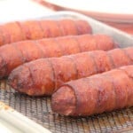 A row of bacon-wrapped sausages rest after being cooked and glazed.