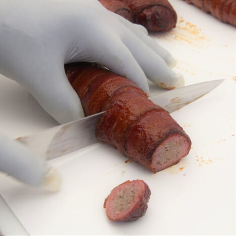The Bacon-wrapped sausage being sliced into serving sizes.