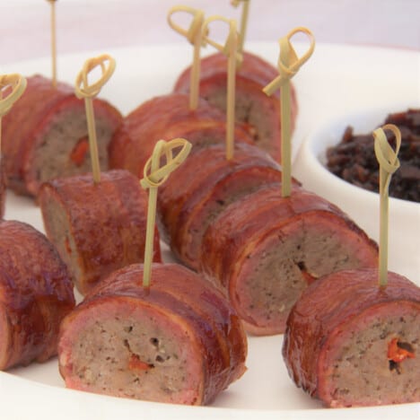 Bacon-wrapped sausages are sliced and a toothpick added ready to be served as a finger food.