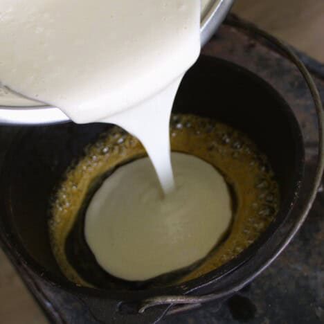 Pancake mixture being poured into a Dutch oven with a base of warmed golden syrup.