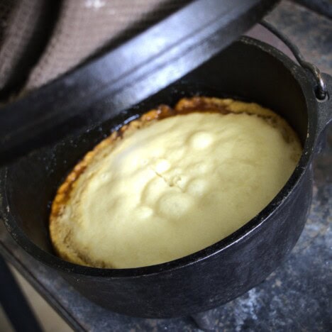 Lid being taken off a Dutch oven to show a baked golden syrup pudding.