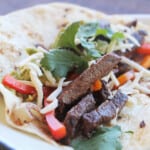 Close up of fajitas highlighting the beef, bell pepper, cheese, and cilantro garnish.
