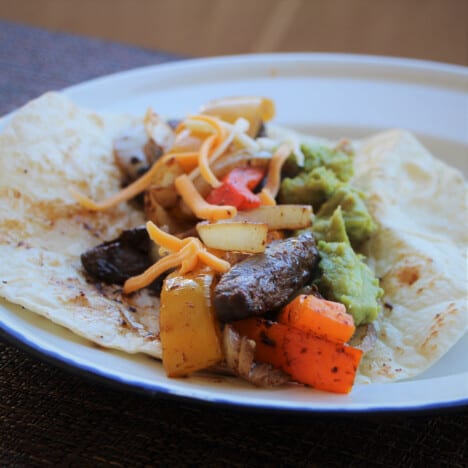 A plate with a tortilla laid flat topped with all the fajita elements.