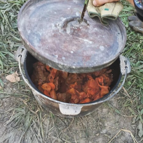 The lid being taken off the Dutch oven with campfire beef stew in it.