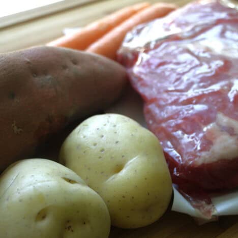 Raw vegetables of potato, sweet potato, and carrots with a vacuum-packed corned beef.
