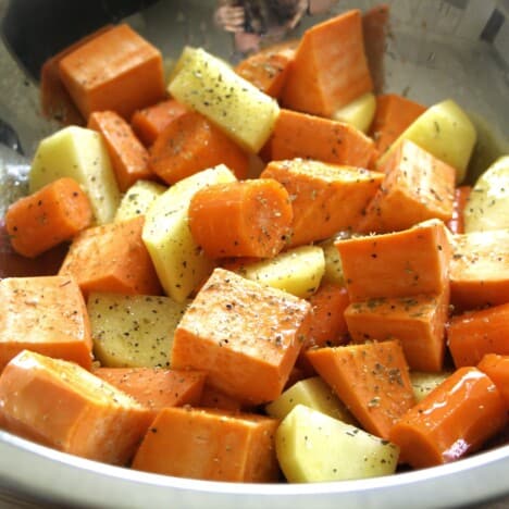 Close up on seasoned cubed carrot, sweet potato, and potato.