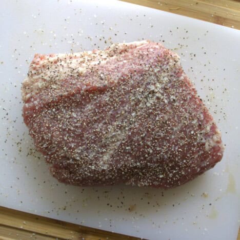 Corned beef on a white chopping board seasoned with salt and pepper.
