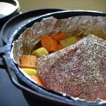 A foil lined Dutch oven with a seasoned corned beef and vegetables ready to cook.