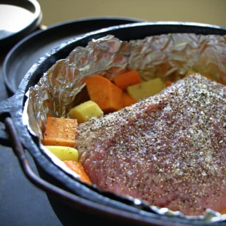 A foil lined Dutch oven with a seasoned corned beef and vegetables ready to cook.