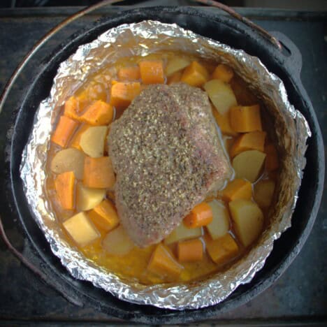 A Dutch oven with a foil lining containing a roast beef and vegetables.