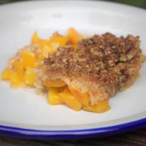 A serving of peach crisp on a white camp plate.