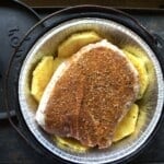 Looking down on a Dutch oven with a foil liner filled with pineapple slices topped with a piece of rubbed pork.