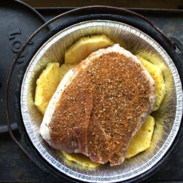 Looking down on a Dutch oven with a foil liner filled with pineapple slices topped with a piece of rubbed pork.