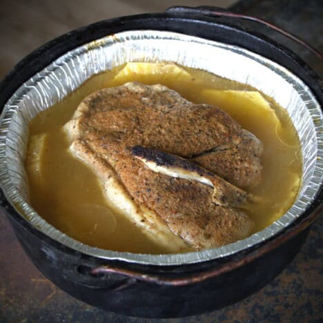 A lined Dutch oven with a cooked piece of pork and multiple slices of pineapple in a liquid.