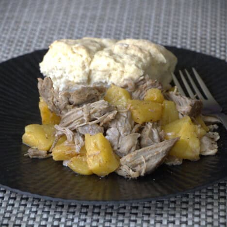 A black camp plate with pineapple pork and a biscuit.
