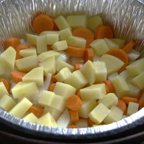 A lined Dutch oven filled with cubed potato, carrot and onion.