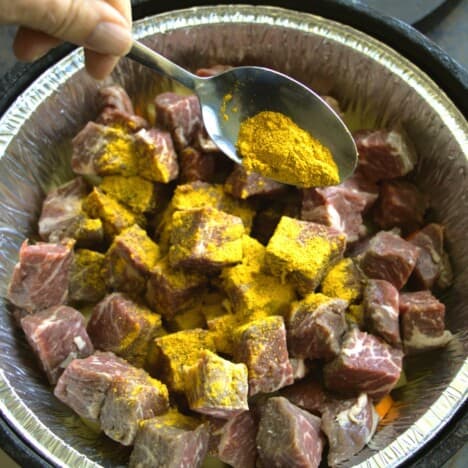 Dutch oven with a liner filled with meat and veg having a spoonfull of curry powder sprinkled over it.