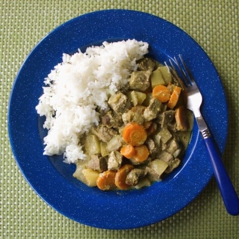 Blue camp plate with a serving of yellow beef and vegetable curry and a side of white rice.