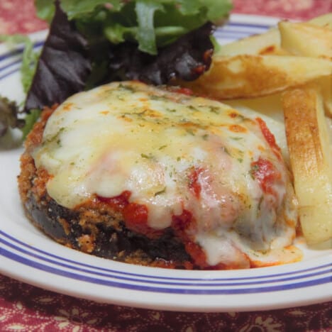 An eggplant parma with melted cheese sits on a plate next to a green salad.