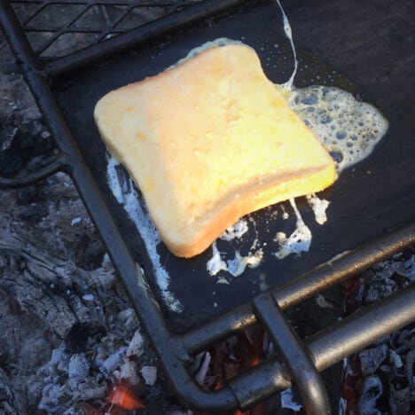 A slice of uncooked french toast cooking in a skillet.