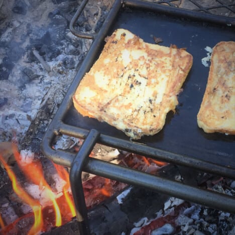 Two cooked pieces of French toast on a skillet over hot coals.