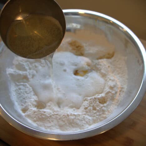 Ginger beer being poured into a stainless bowl with flour in it.