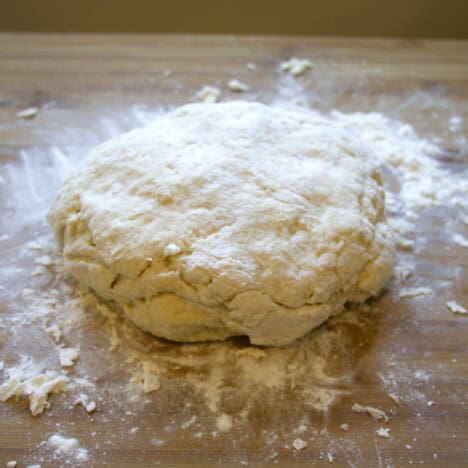 Ball of dough on a wooden board dusted with four.