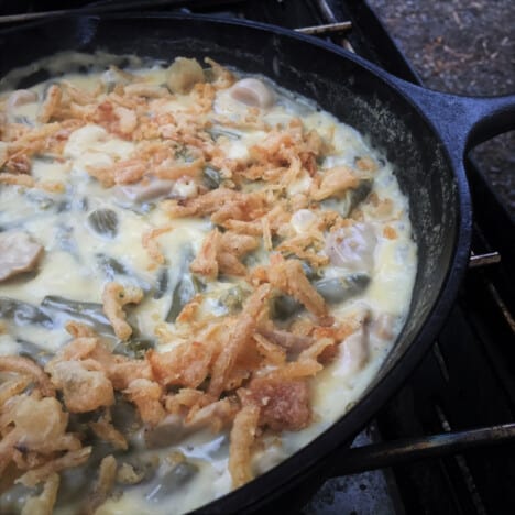 Green beans in a thick sauce are in a skillet sprinkled with crispy fried onions.
