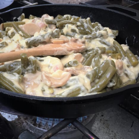 Green bean casserole cooking in a skillet on a gas stove top.