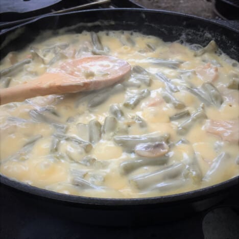 Green beans and mushrooms are cooking in a rich and thick cream sauce in a skillet.
