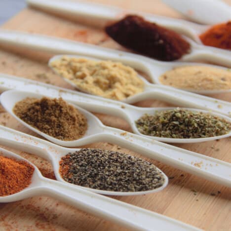 Looking at an angle over white spoons filled with various spices.