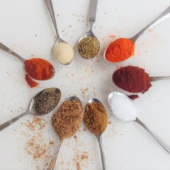 Looking down onto a circle of teaspoons each with a different spice in it.