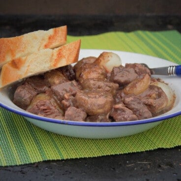 Looking across a white shallow bowl of Beef Bourguignon with two slices of baguette bread.