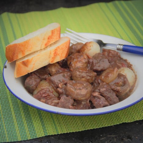 A white bowl of beef Bourguignon served with two slices of bread and a fork.