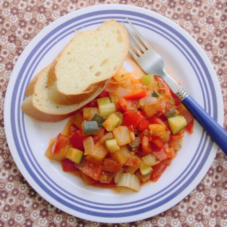 Looking down on a camp plate with a hearty serving of ratatouille with fresh bread.