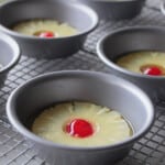 Mini round baking dishes with pineapple rings and a cherry in the middle of the pineapple hole.
