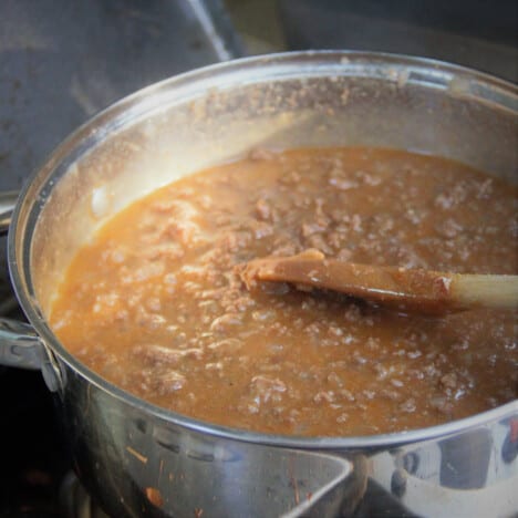 A large pot with the cooking beef base being stirred by a wooden spoon.