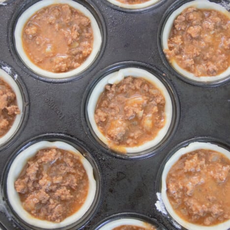 Looking down into a muffin tin filled with pastry and beef filling.
