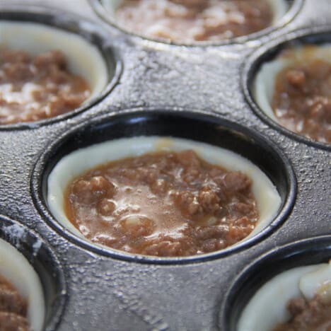 A muffin pan holds individual unbaked portions of mini meat pies.