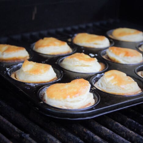 A muffin tin is filled with baked mini meat pies with golden brown crust.