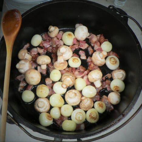 Looking down into a Dutch oven with cooked mushrooms and pearl onions.