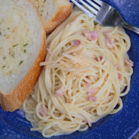 Looking down onto a blue plate with a serving of pasta carbonara and a side of garlic bread.
