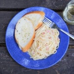 Arial view of a blue camping plate with a serving of pasta carbonara and two slices of garlic bread.