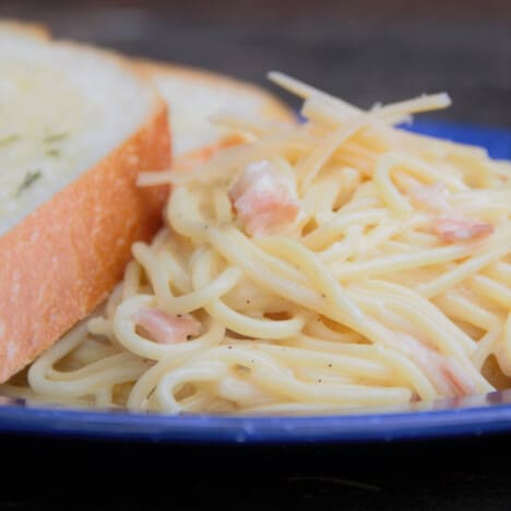 A blue plate with pasta carbonara and a side of garlic bread.