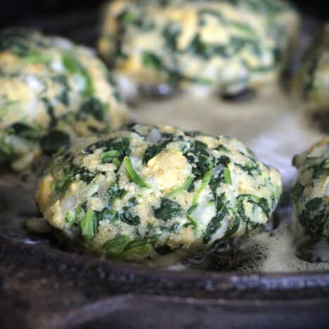 Close up of a spinach patty frying in a skillet.