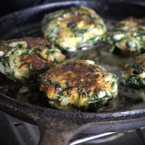 Skillet with spinach patties cooking in it.