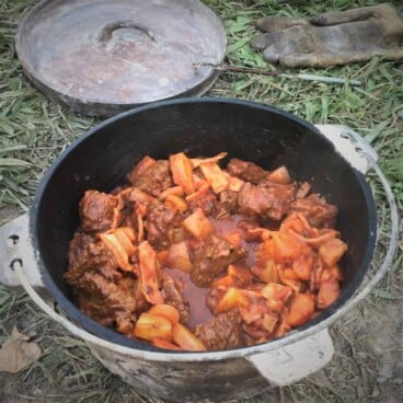 Close up of campfire beef stew in a Dutch oven showing the beef, potatoes, and carrots.