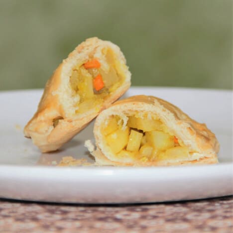 A vegetable pastie on a white plate cut in half showing the filling.